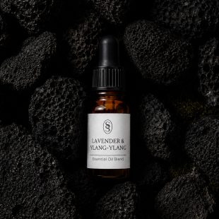 Lavender & Ylang-Ylang pure essential oil blend bottle resting on natural lava stones