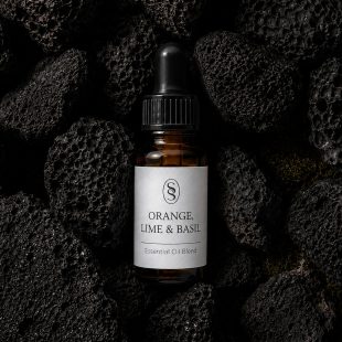 Orange, Lime & Basil pure essential oil blend bottle resting on natural lava stones