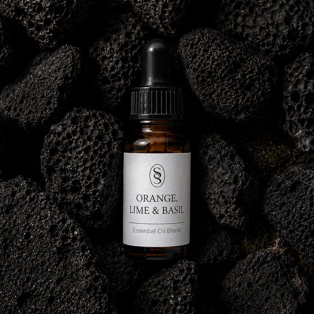 Orange, Lime & Basil pure essential oil blend bottle resting on natural lava stones